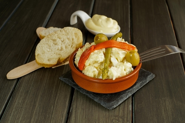 Tapa de ensaladilla rura or russian salad typical spanish tapa in a clay pot garnished with red bell pepper, asparagus and olives