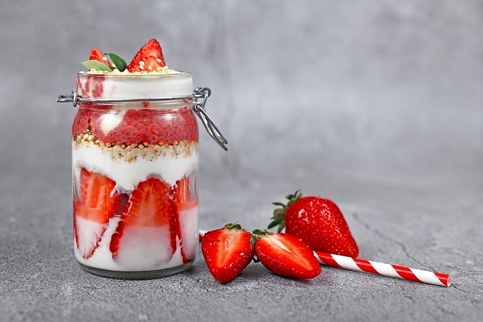 Strawberry fruit dessert with low fat yogurt, chia seeds and puffed quinoa grains layered in jar surrounded by berries