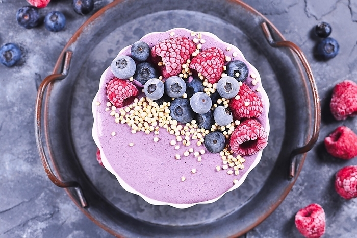 Fruit smoothie bowl with pink yogurt decorated with healthy raspberry, blueberry and puffed quinoa grain on iron tray