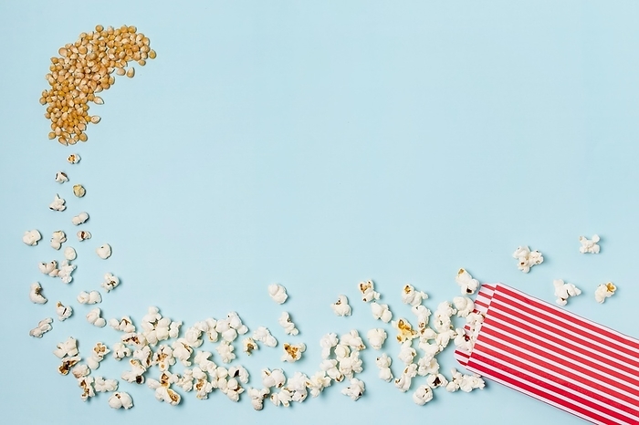 Corn seeds turns into popcorns enter popcorn box against blue backdrop