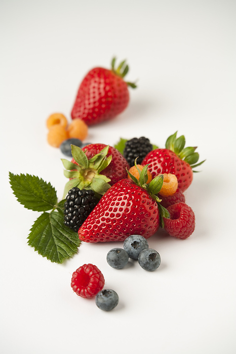 Agriculture - Mixture of berries: strawberries, red and golden raspberries, blackberries and blueberries with leaves, on white., by Ed Young / Design Pics