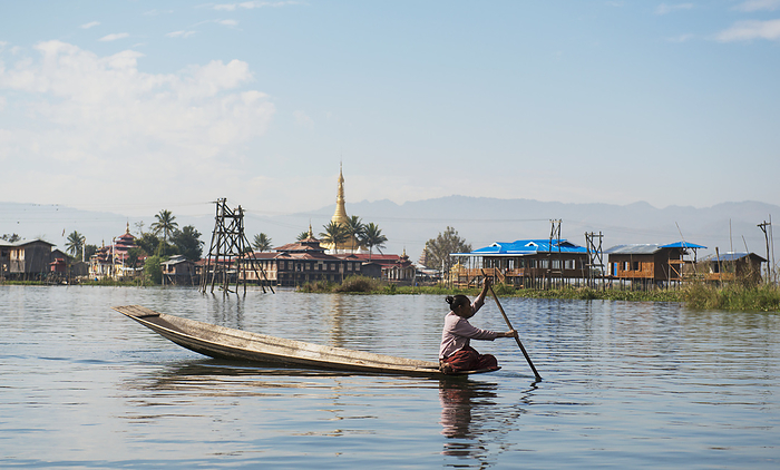 Myanmar A Woman Sits On The Edge Of Her Boat Paddling To Shore With A Temple In The Distance  Taungyii, Shan State, Myanmar, by Stuart Corlett   Design Pics