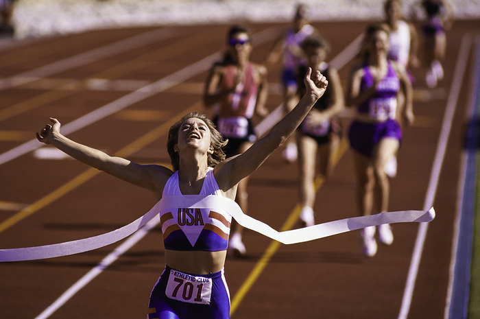 Track and Field Female runner victorious at the finish line in a track race.