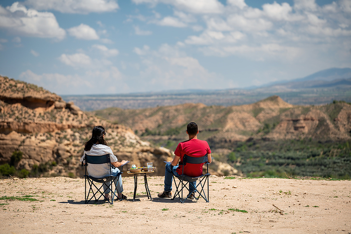 Couple sit on chairs with a table looking at a desert like landscape near Francisco Abellan Dam, Granada, Andalusia, Spain, Europe Couple sit on chairs with a table looking at a desert like landscape near Francisco Abellan Dam, Granada, Andalusia, Spain, Europe, by Luis Pina