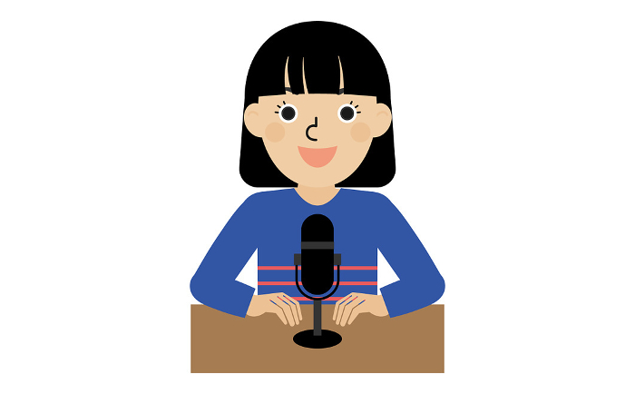 A dark-haired Japanese woman in long-sleeved clothing speaking into a stand microphone in front of a desk