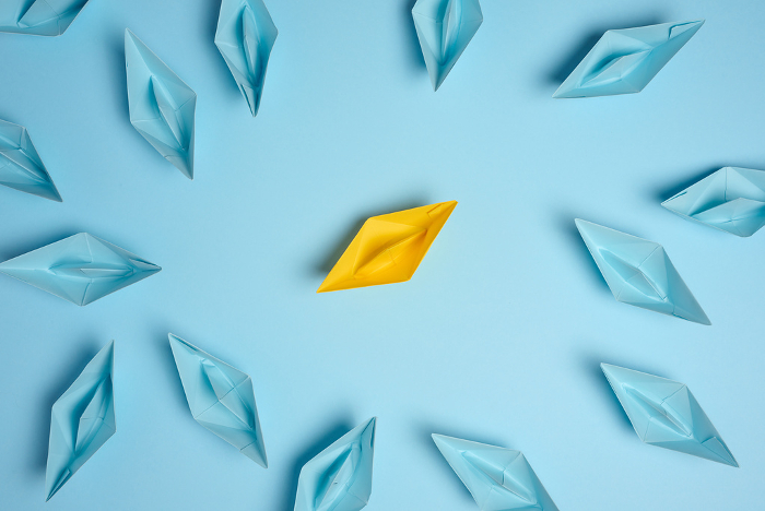 A group of blue paper boats surrounded one yellow boat, the concept of bullying, search for compromise. Top view A group of blue paper boats surrounded one yellow boat, the concept of bullying, search for compromise. Top view