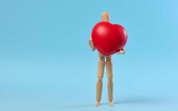 A wooden mannequin holding a red heart on a blue background, symbolizing the concept of blood and organ donation A wooden mannequin holding a red heart on a blue background, symbolizing the concept of blood and organ donation