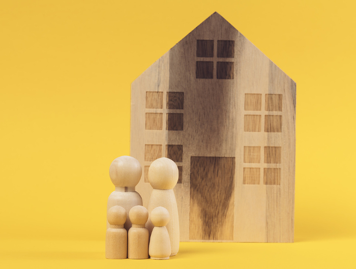 Wooden house and miniature figurines of a family on a yellow background. The concept of selling and buying real estate, investment Wooden house and miniature figurines of a family on a yellow background. The concept of selling and buying real estate, investment