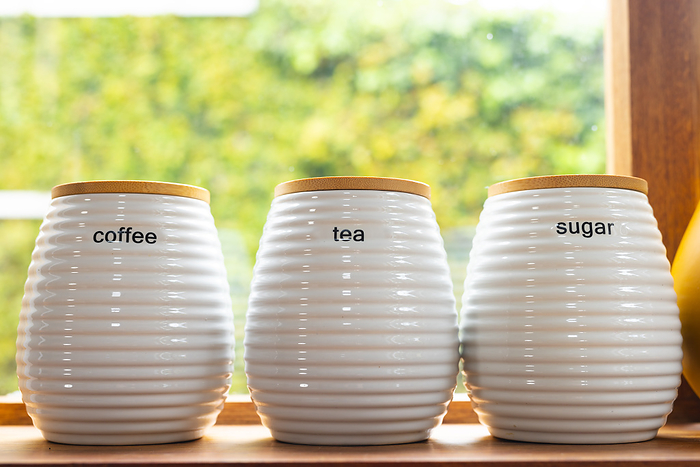 Matching coffee, tea and sugar storage jars on windowsill in kitchen, copy space. Beverages, storage, organisation, domestic life and lifestyle.