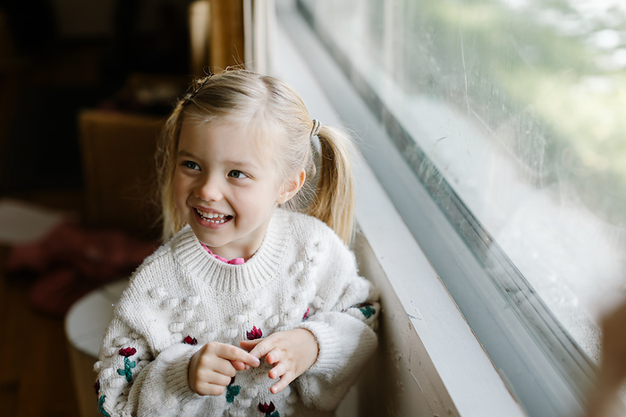 Animated toddler next to a window eagerly talks about Santa Claus, by Cavan Images / Aubrey Westlund