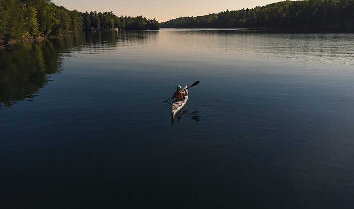 Aerial view of woman paddling kayak on dark blue water of lake., by Cavan Images / Dorene Hookey