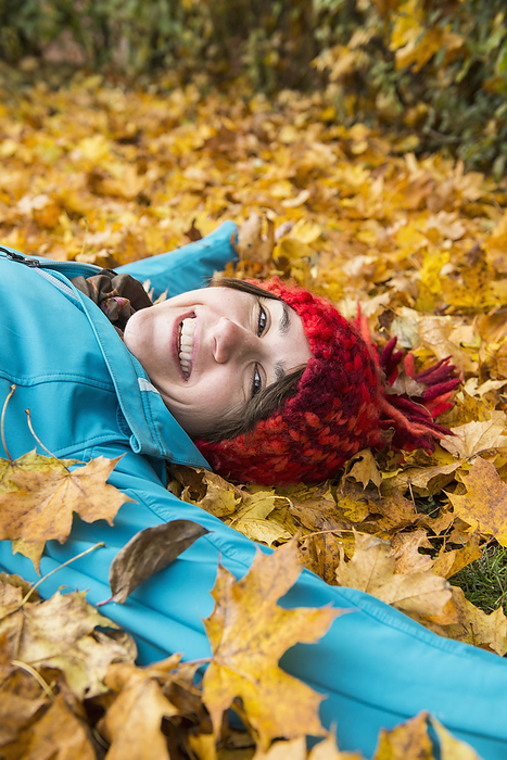 smiling woman lying on the ground in a heap of autumn leaves Smiling woman lying on the ground in heap of autumn leaves, by Cavan Images   Edith Drentwett