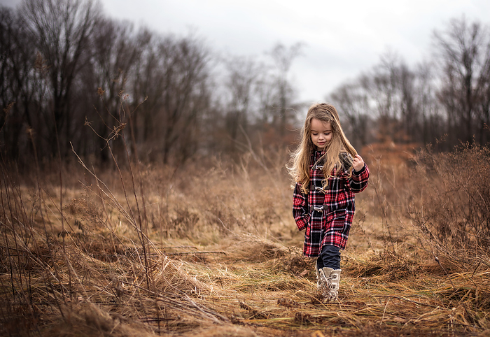 Little girl with long curly hair walking through field in autumn, by Cavan Images / Joy Faith
