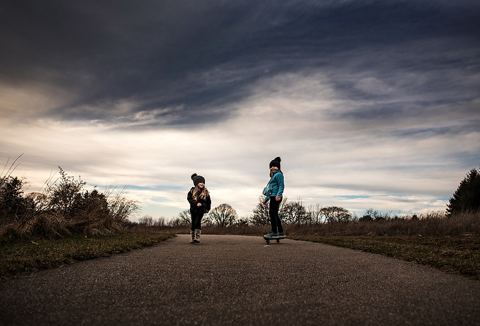 Sisters skateboarding under blue sky, by Cavan Images / Joy Faith