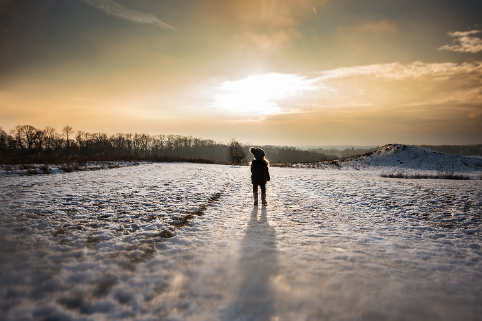 Little girl standing alone in snowy field at sunset, by Cavan Images / Joy Faith