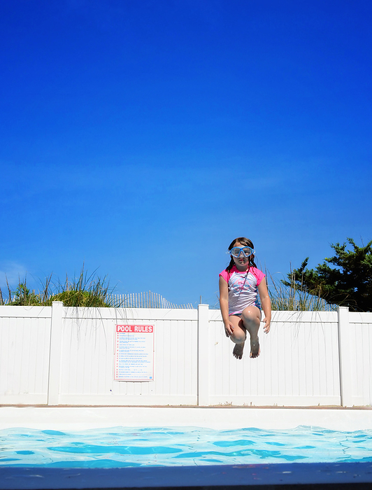 Young girl wearing goggles jumping into pool, by Cavan Images / Joy Faith