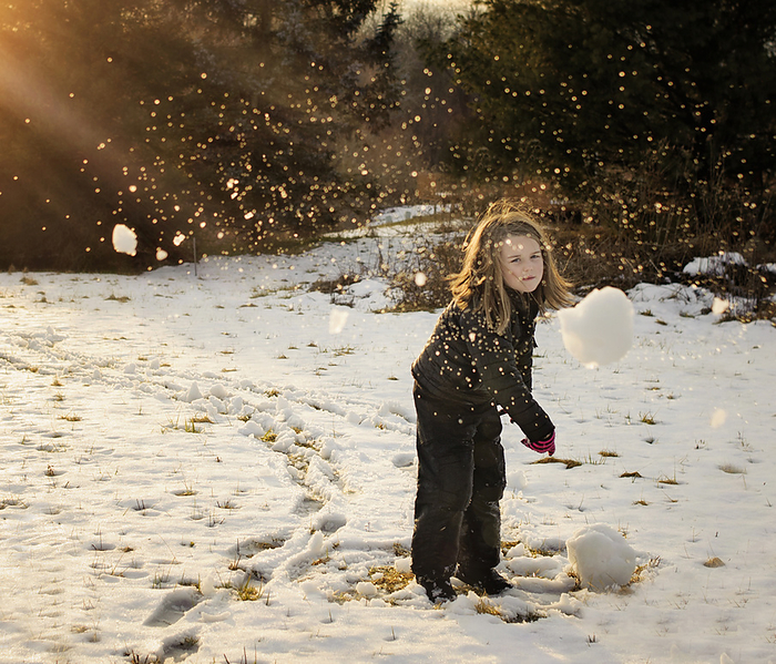Young girl throwing snowball outdoors in winter, by Cavan Images / Joy Faith