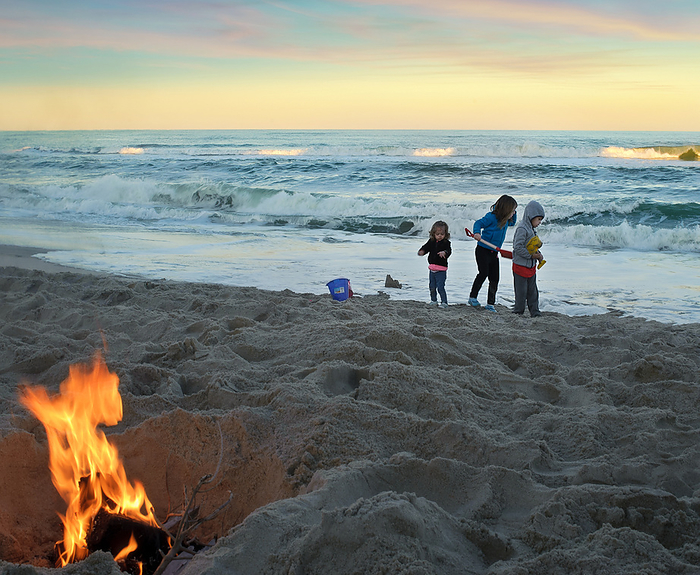three young children playing in sand with bonfire, by Cavan Images / Joy Faith