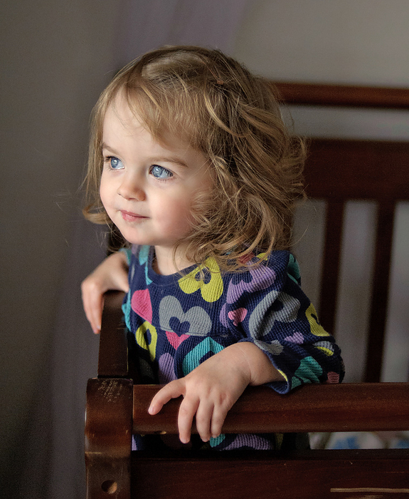 Beautiful toddler with blue eyes standing in crib, by Cavan Images / Joy Faith