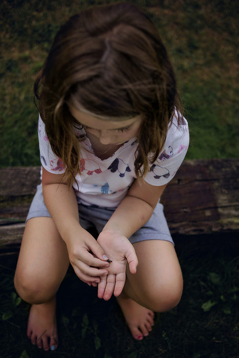 Little girl holding bug outdoors in summer, by Cavan Images / Joy Faith