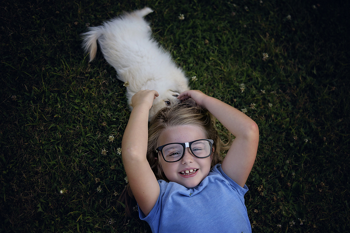 Little girl with glasses playing with white pomeranian, by Cavan Images / Joy Faith