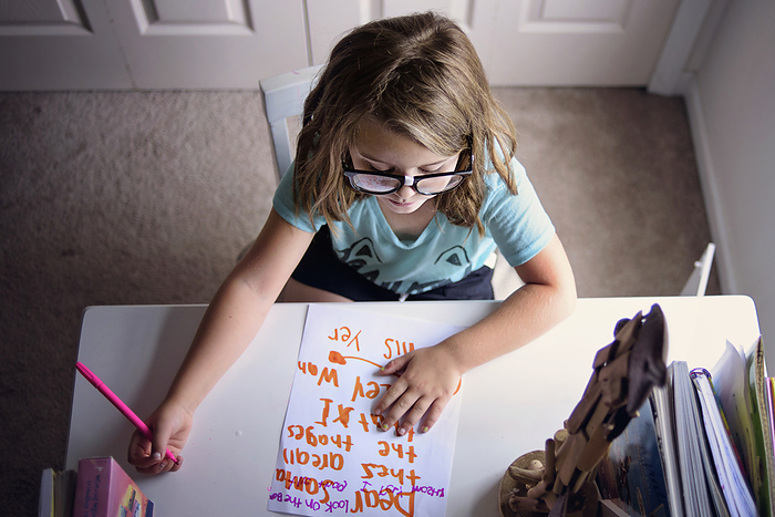 Little girl with glasses writing letter to Santa, by Cavan Images / Joy Faith
