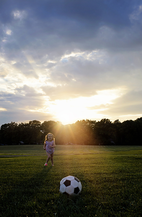 Little girl smiling and running toward soccer ball, by Cavan Images / Joy Faith