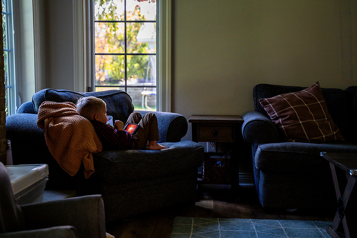 Toddler Boy Lounging On Oversized Chair Watching Show on Cell Phone, by Cavan Images / Alyxandra Walton