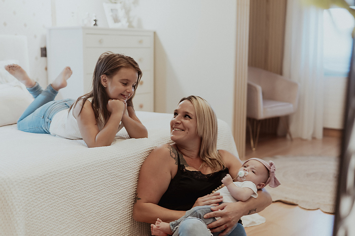Portrait of smiling girl with mother and sister at home, by Cavan Images / Paula Berezo