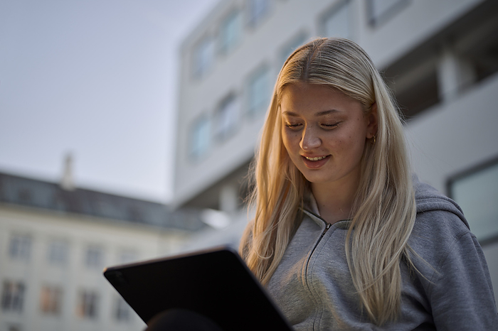 Smiling blond woman using tablet in city, by Cavan Images / Oscar Bjarnason