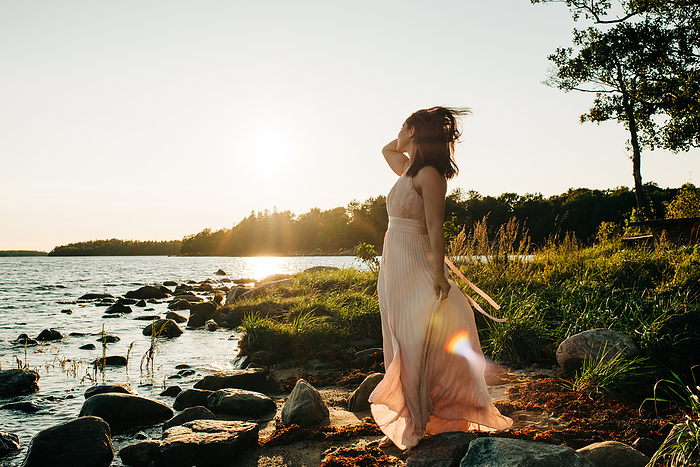 woman by the sea in a beautiful dress and hair blowing in the wind, by Cavan Images / Rachel Bell