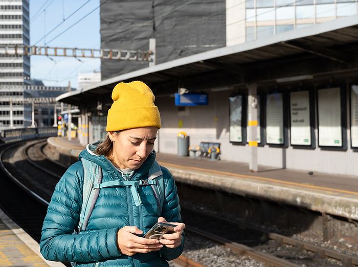 Traveler backpacker woman with her mobile phone at the train station, by Cavan Images / Simon Izquierdo