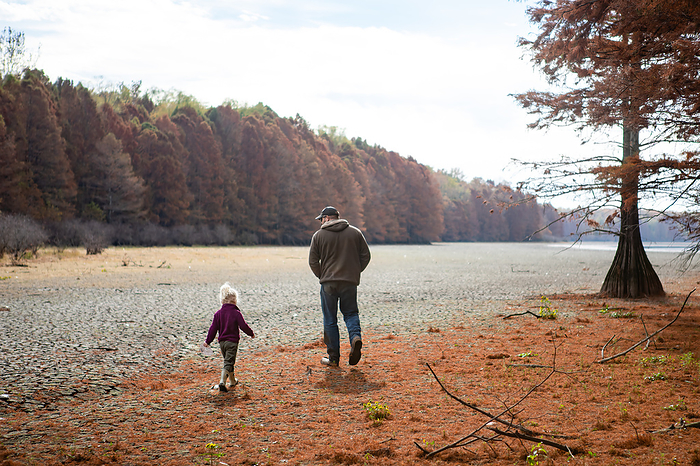 Dad and daughter on nature walk along lake during autumn day, by Cavan Images / Krista Taylor