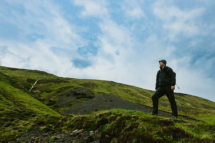 Man on top of green mountain hiking with blue skies, by Cavan Images / Anna Rasmussen Photographs