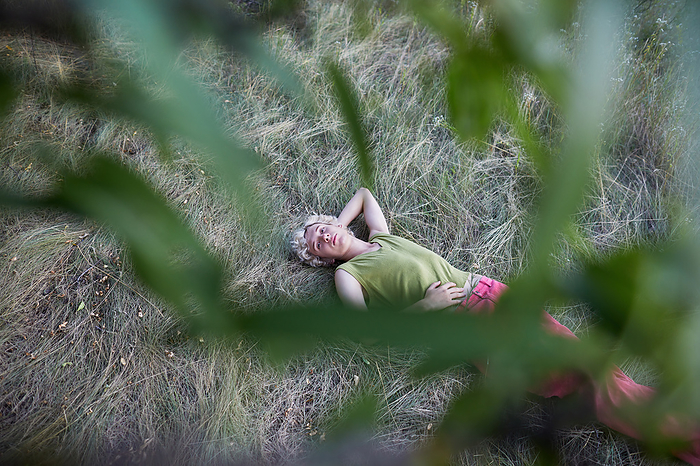 young guy relaxing on the grass, top view through the foliage, by Cavan Images / Elena Perevalova