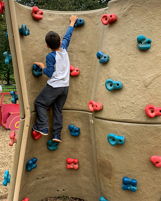Young boy playing on climbing wall suburban playground., by Cavan Images / Sara Taylor