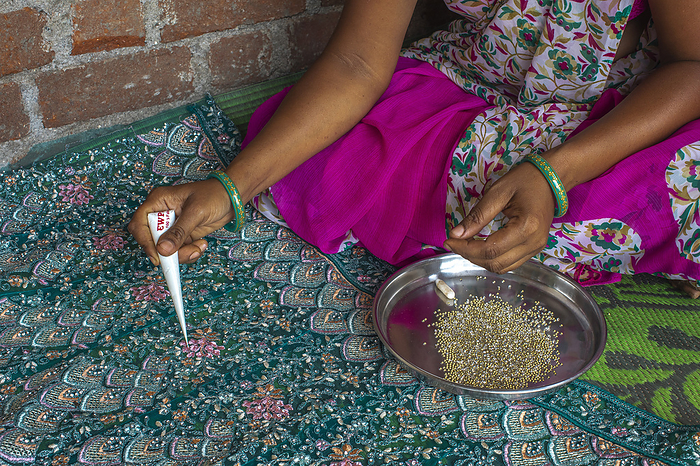 Adivasi woman sticking beads onto a sari in a village in Narmada district, Gujarat, India, Asia Adivasi woman sticking beads onto a sari in a village in Narmada district, Gujarat, India, Asia, by Godong