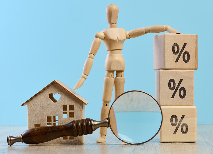 Wooden dummy, house and a magnifying glass, representing the concept of real estate purchase, rental growth, and mortgage interest Wooden dummy, house and a magnifying glass, representing the concept of real estate purchase, rental growth, and mortgage interest