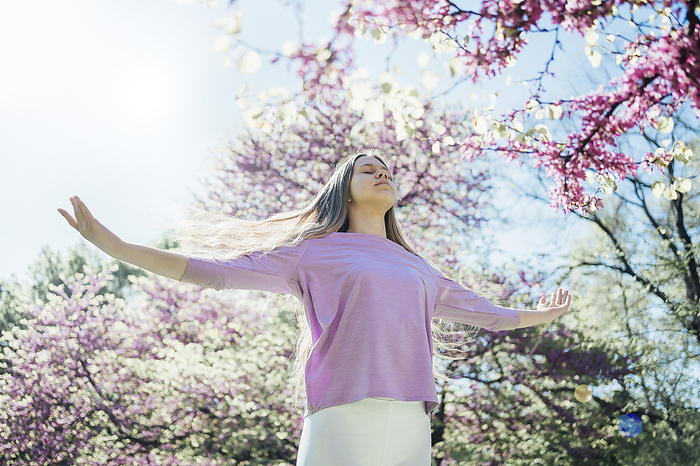 Teenage girl with arms outstretched practicing yoga at park in bloom