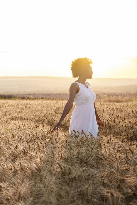 Young woman wearing white dress standing in wheat field at sunset