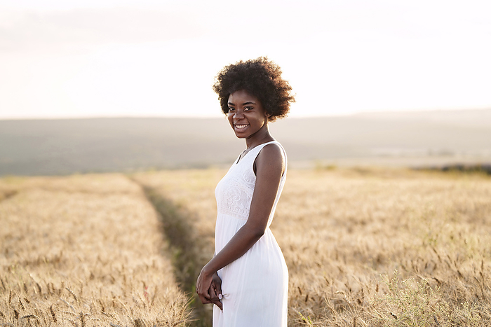Happy young woman standing in wheat field at sunset