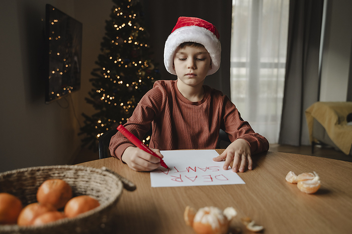 Boy wearing santa hat writing on paper at table