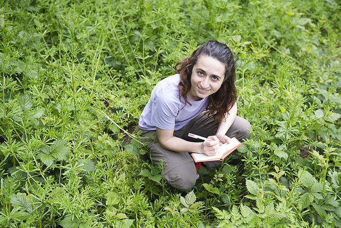Happy environmentalist crouching with book amidst plants