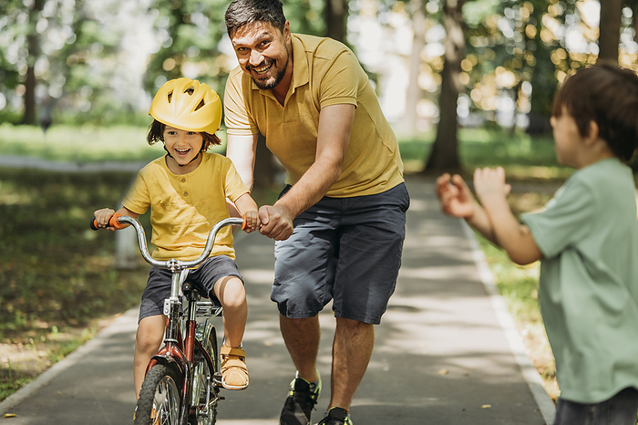 Smiling father helping son to ride bicycle in park