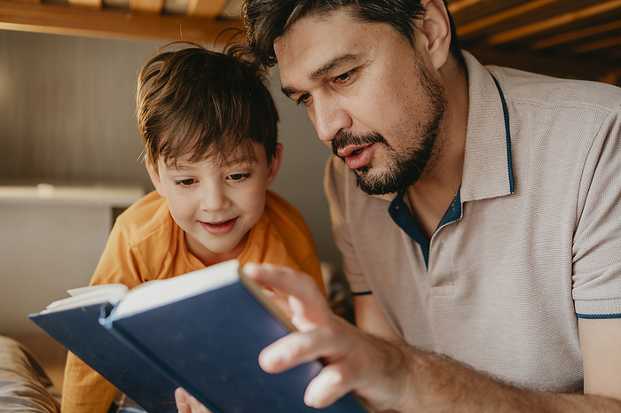 Father reading book to son in bedroom at home
