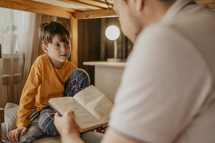 Father reading book to son in bunk bed at home
