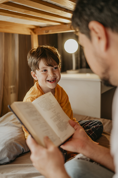 Father reading book to happy son in bunk bed at home