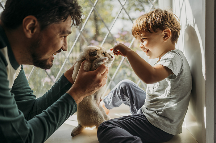 Happy father holding puppy in front of boy at home