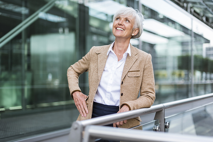 Smiling senior businesswoman leaning on railing in the city looking up