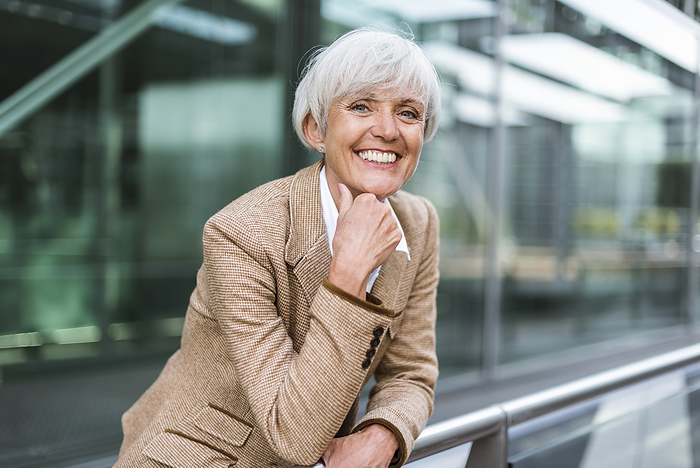 Portrait of smiling senior businesswoman leaning on railing in the city